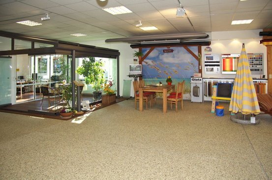 Ausstellungsraum mit Wintergarten, Terrassenmöbeln, Sonnenschirm und Farbmuster-Displays.