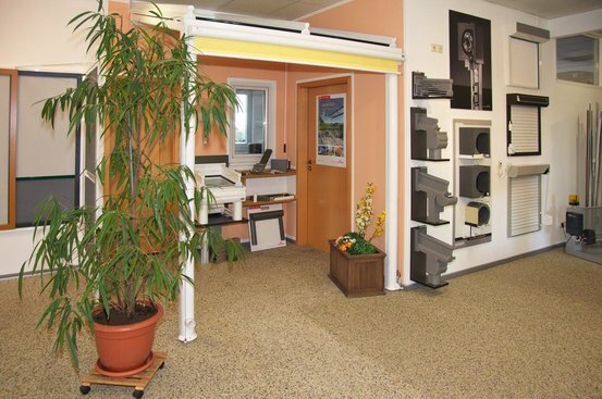 Ausstellungsraum für Rollläden und Markisen mit Pflanzen und Musterstücken an der Wand.